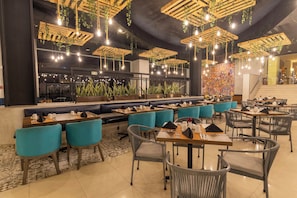 Un restaurante con varias zonas de estar, incluyendo cabinas y mesas, con lámparas colgantes y plantas.