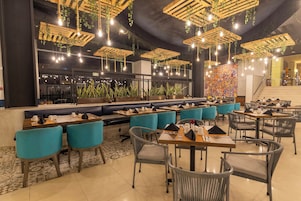 Un restaurante con varias zonas de estar, incluyendo cabinas y mesas, con lámparas colgantes y plantas.