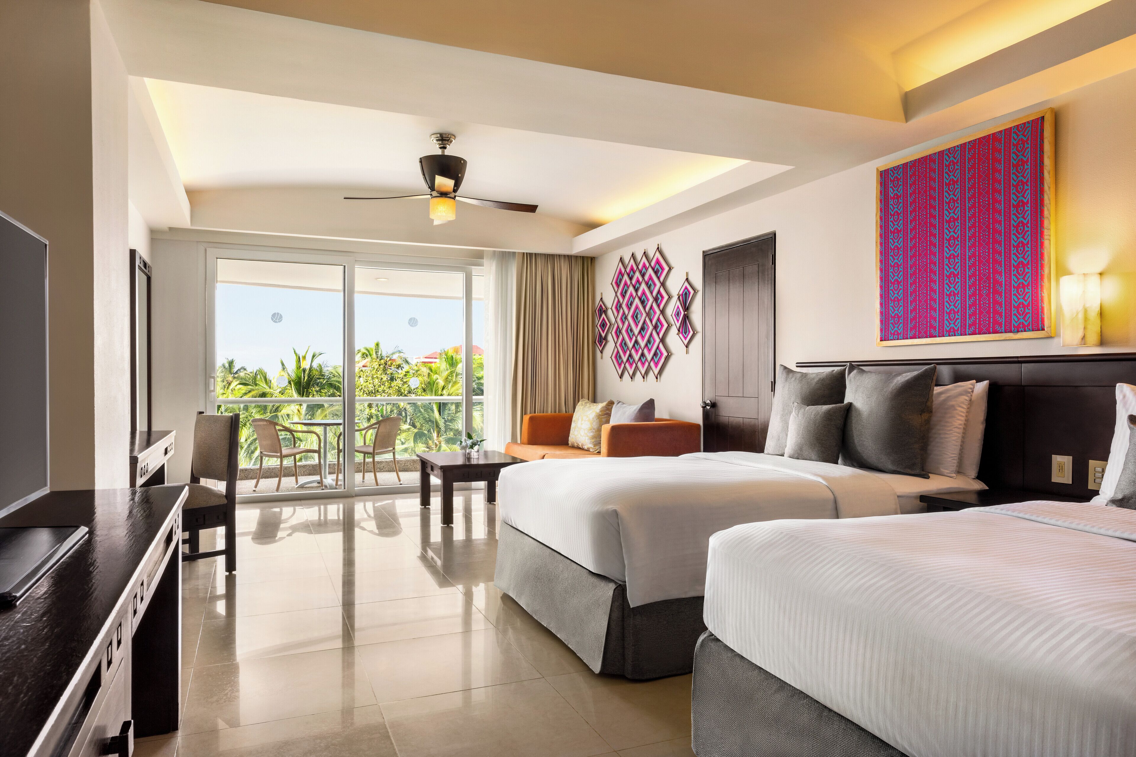 A hotel room with two beds, a balcony with a view, a ceiling fan, and a decorative wall piece.