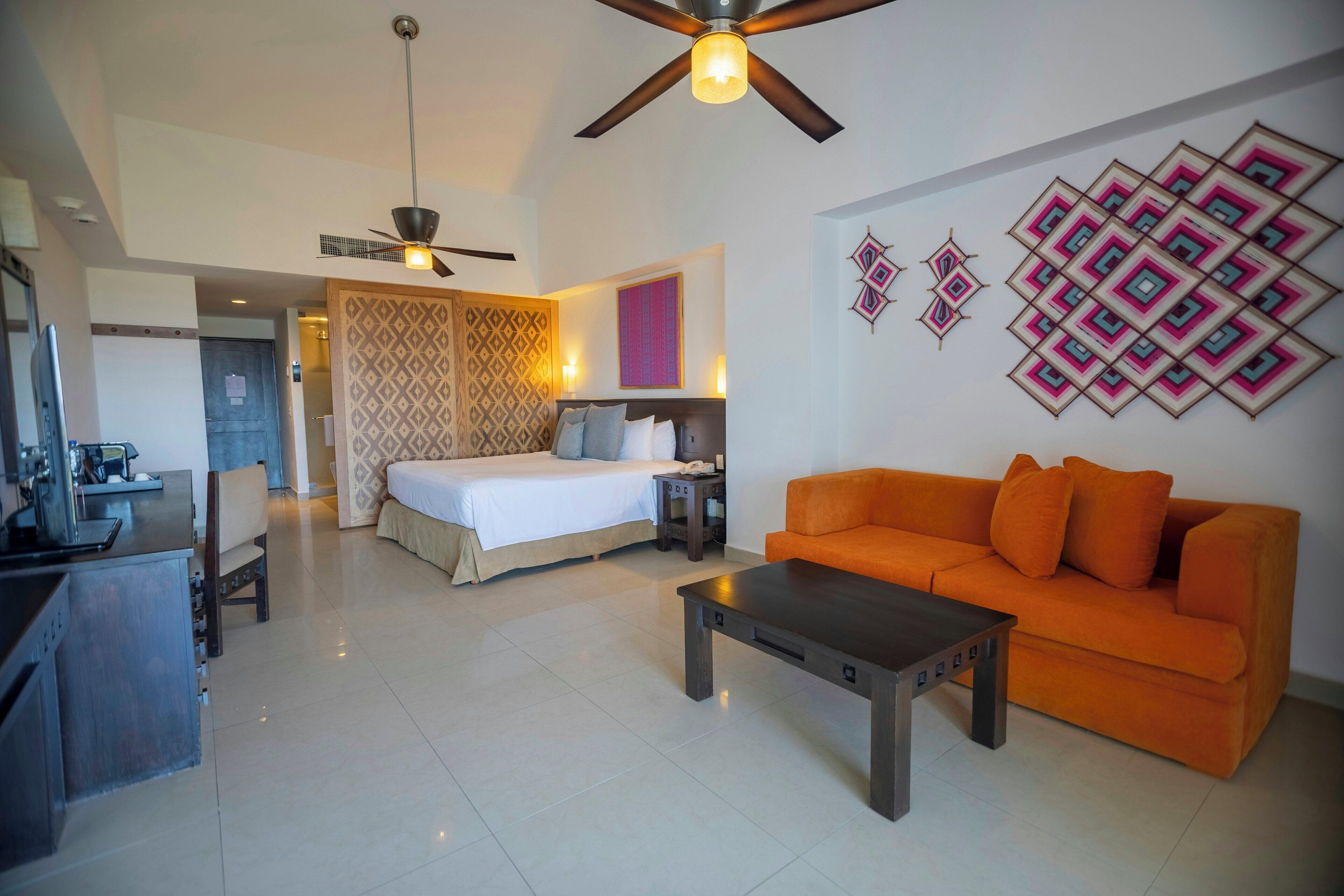 A hotel room with a bed, a sofa, a coffee table, a desk, and a ceiling fan.