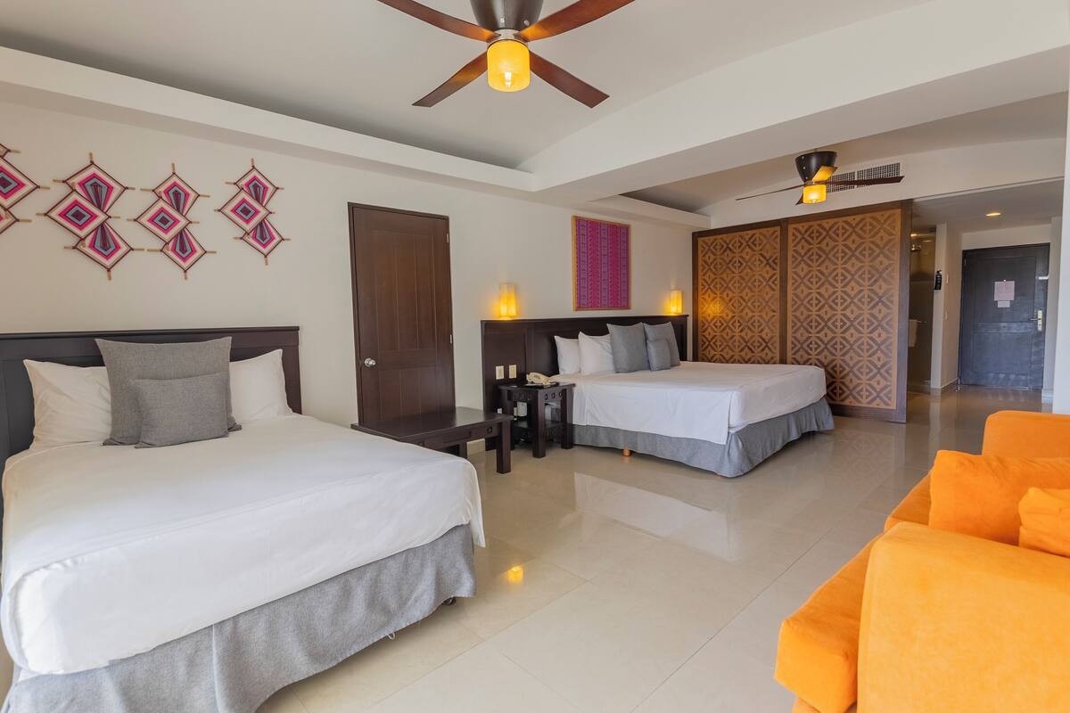 A hotel room with two beds, a sofa, a ceiling fan, and a patterned wall.