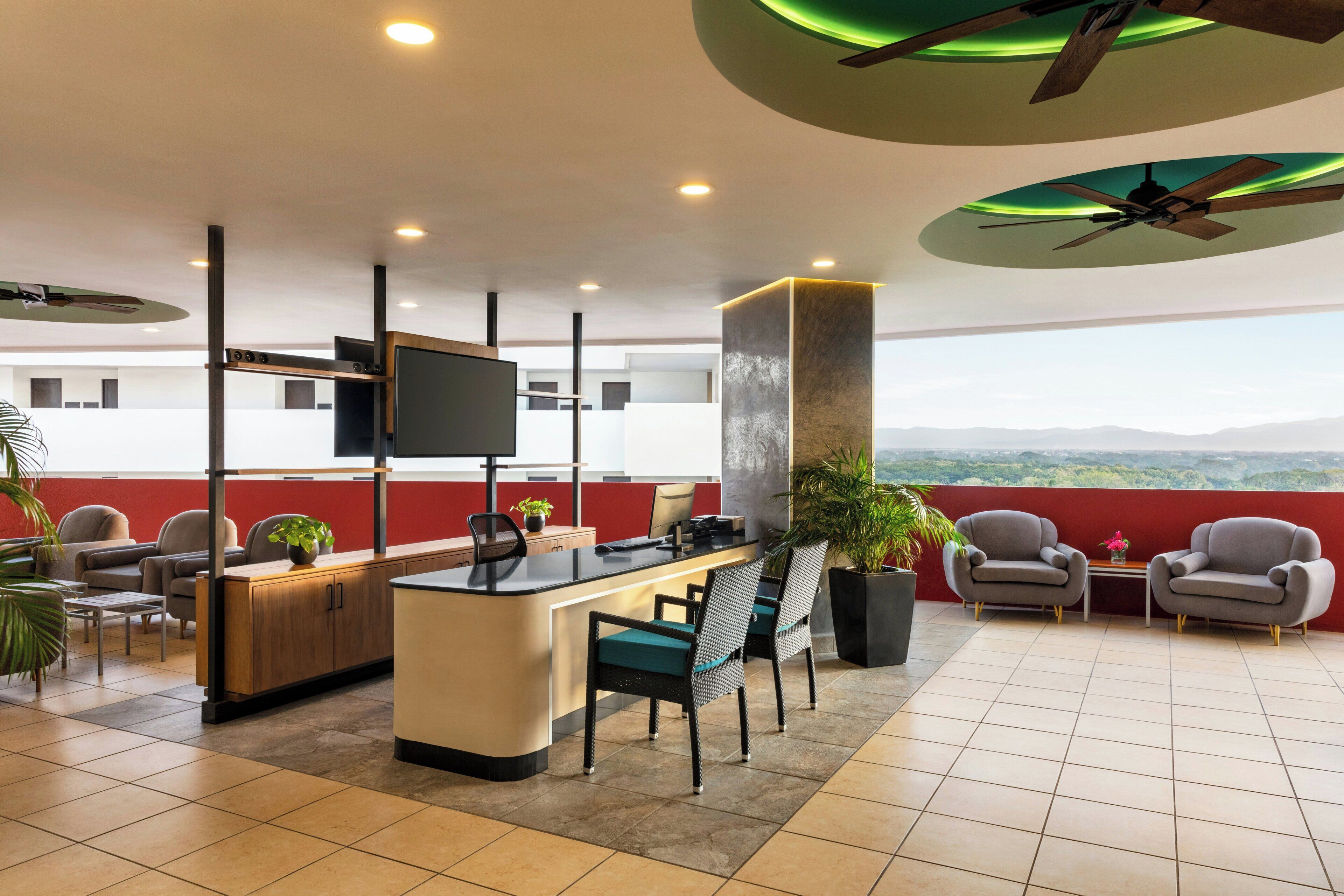 A modern hotel lobby with a reception desk, seating area, and a view of the mountains.