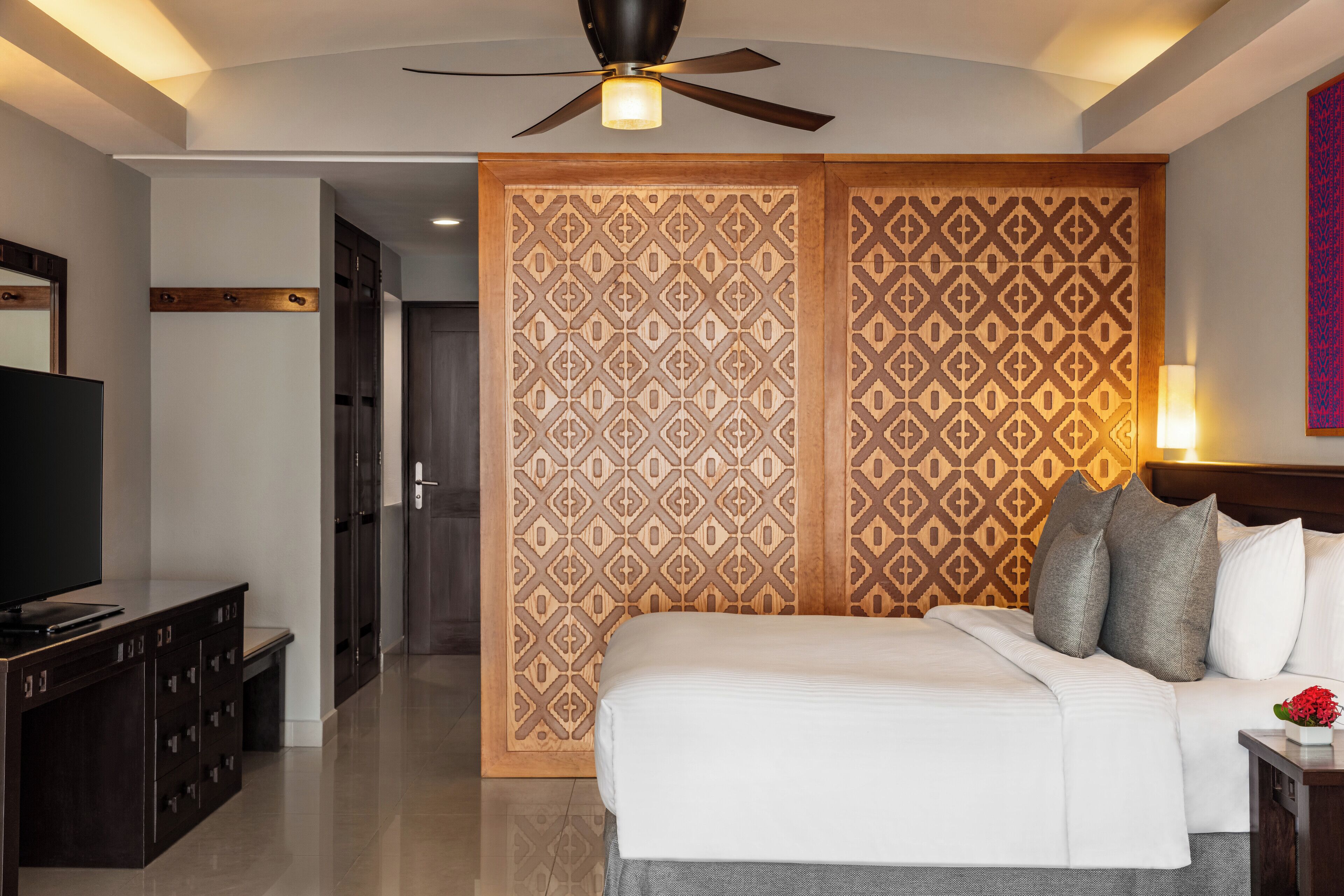 Ein Hotelzimmer mit einem Bett, einem Fernseher, einem Kleiderschrank und einem dekorativen Raumteiler mit geometrischem Muster.
