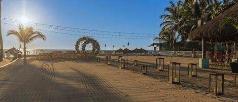 A beach with a clear sky, palm trees, and a thatched-roof structure.