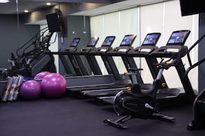 Une salle de sport équipée de tapis de course, de vélos elliptiques et de ballons d’exercice.