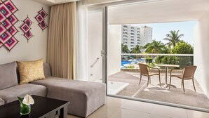 Ein modernes Hotelzimmer mit Balkon, einer Sitzecke, einem Couchtisch und Blick auf einen Pool sowie Gebäude.