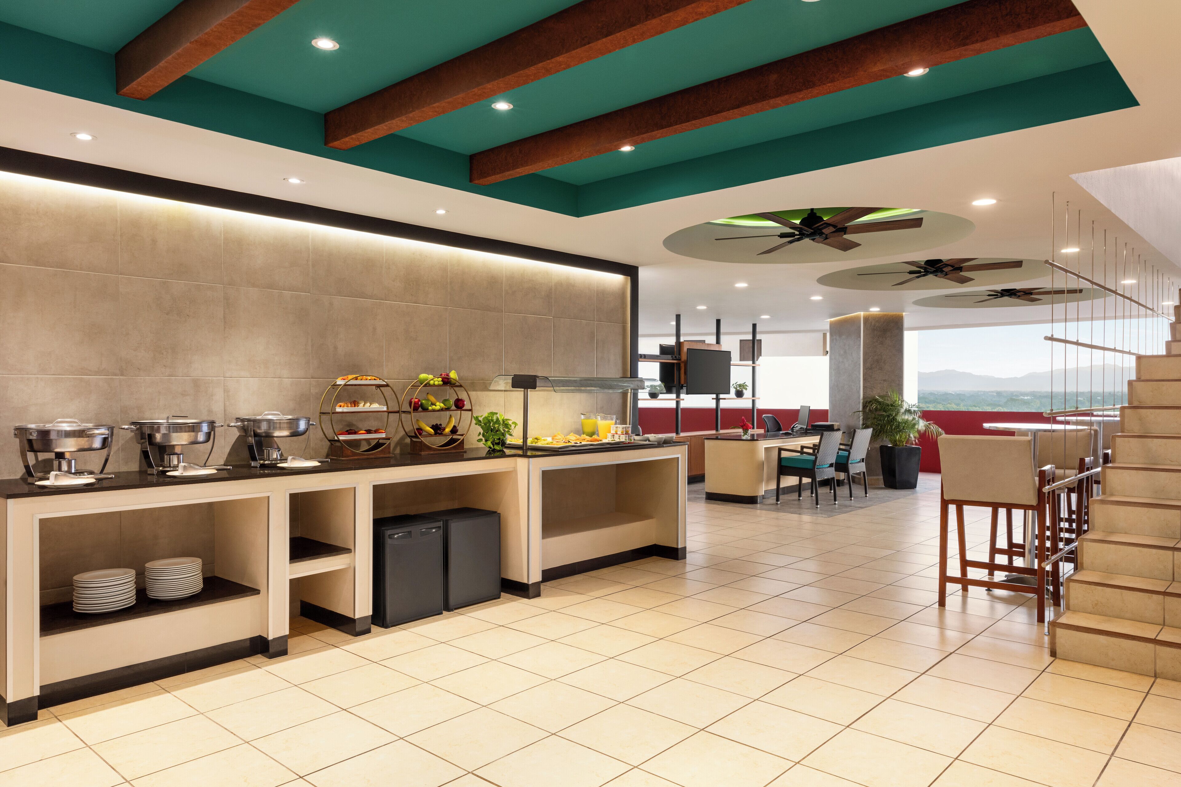 A modern kitchen with a buffet setup, a dining area with chairs, and a staircase leading to an upper level.