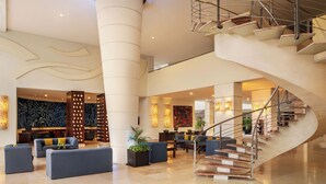 Eine geräumige Lobby mit einer geschwungenen Treppe, Sitzbereichen und einer Rezeption.