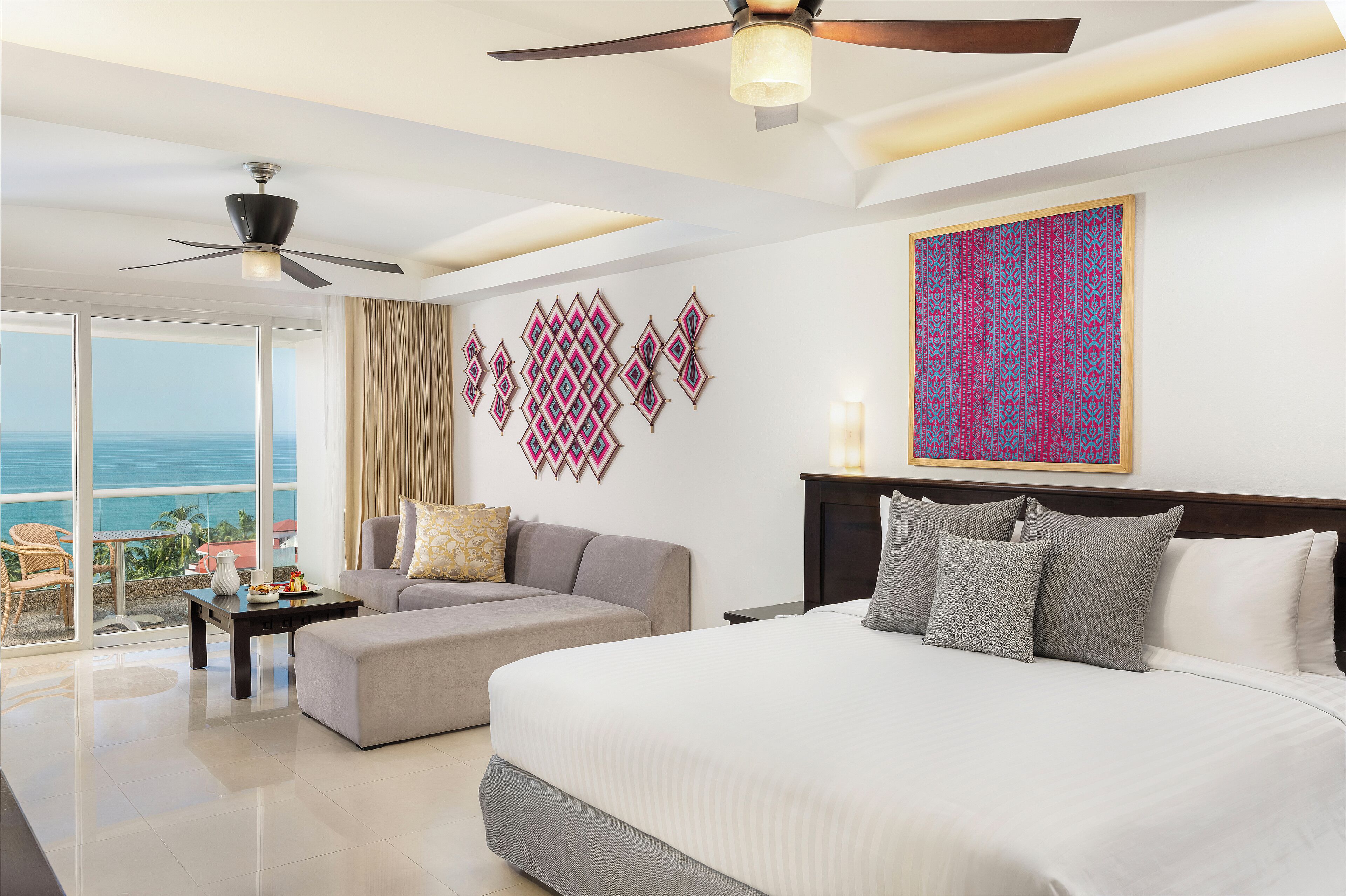 A hotel room with a bed, a sofa, a dining table, and a ceiling fan.