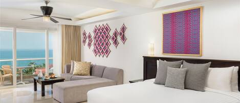 A hotel room with a bed, a sofa, a dining table, and a ceiling fan.