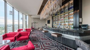 A modern bar area with a high bar counter, red seating, and a patterned carpet. - Southern Sun Sandton (Sandton)