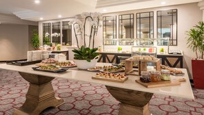 A buffet setup with various food items and a potted plant. - Southern Sun Sandton (Sandton)