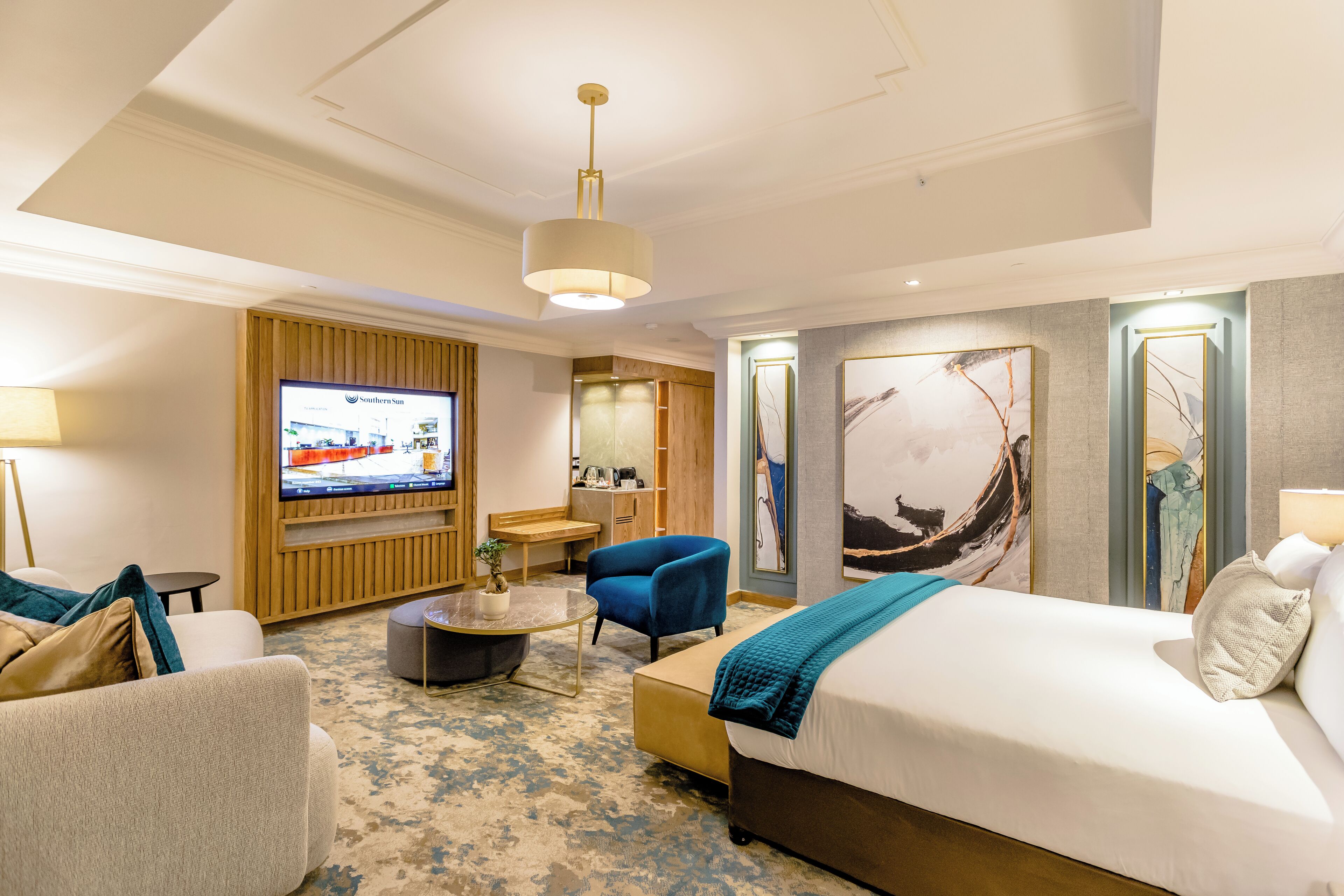 A hotel room with a large bed, a seating area with a coffee table, a TV, and artwork on the walls.