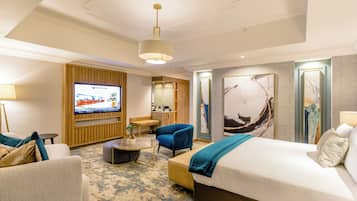 A hotel room with a large bed, a seating area with a coffee table, a TV, and artwork on the walls.