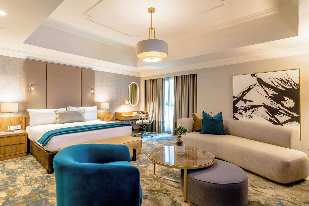 A modern hotel room with a large bed, a sofa, a coffee table, and a desk.