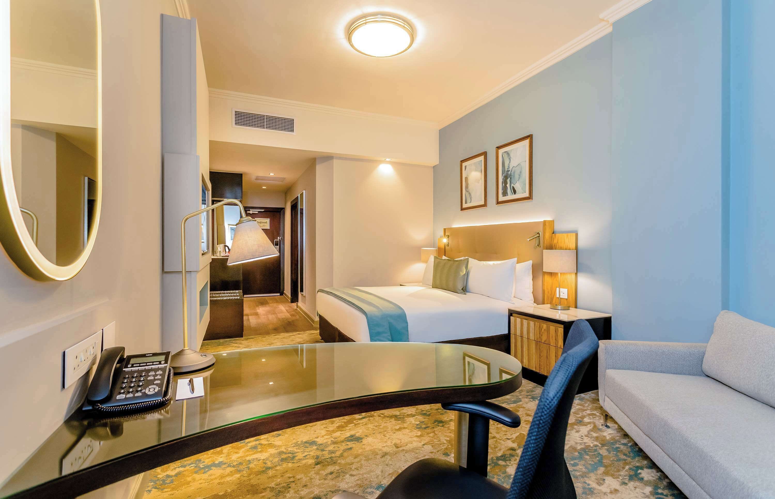 A hotel room with a bed, a desk with a telephone, a chair, a sofa, and a mirror.
