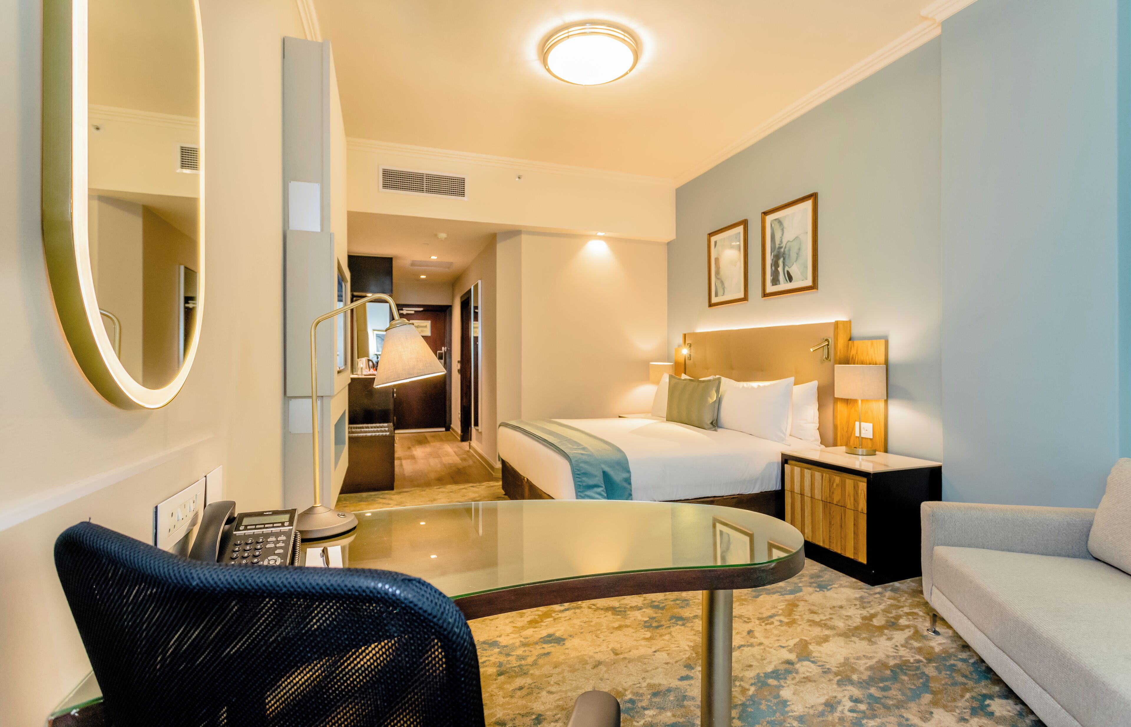 Une chambre d’hôtel comprenant un lit, un bureau avec un téléphone, une chaise, un canapé, une table de chevet avec des lampes et un miroir.