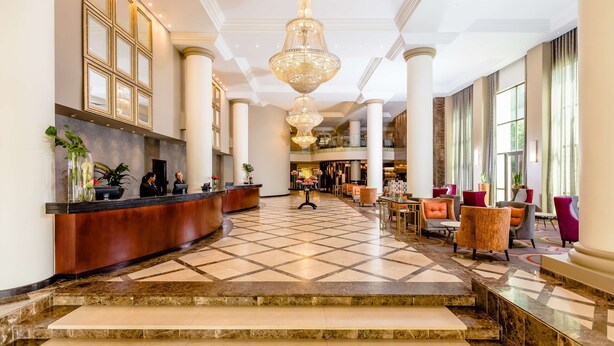 A spacious lobby with a reception desk, a grand chandelier, and a checkered floor. - Southern Sun Sandton (Sandton)