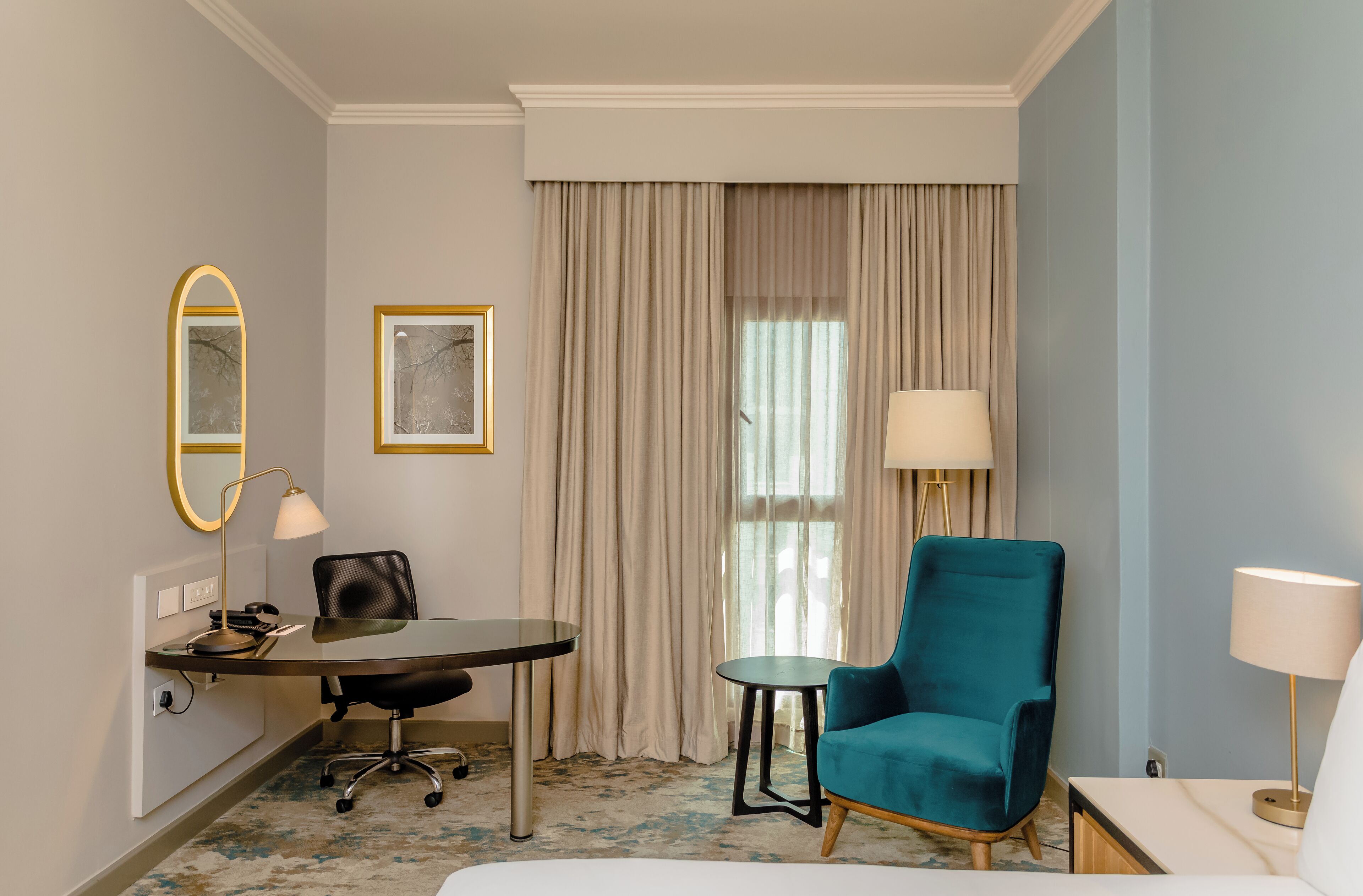 Habitación de hotel con escritorio, silla y un sillón azul verdoso.