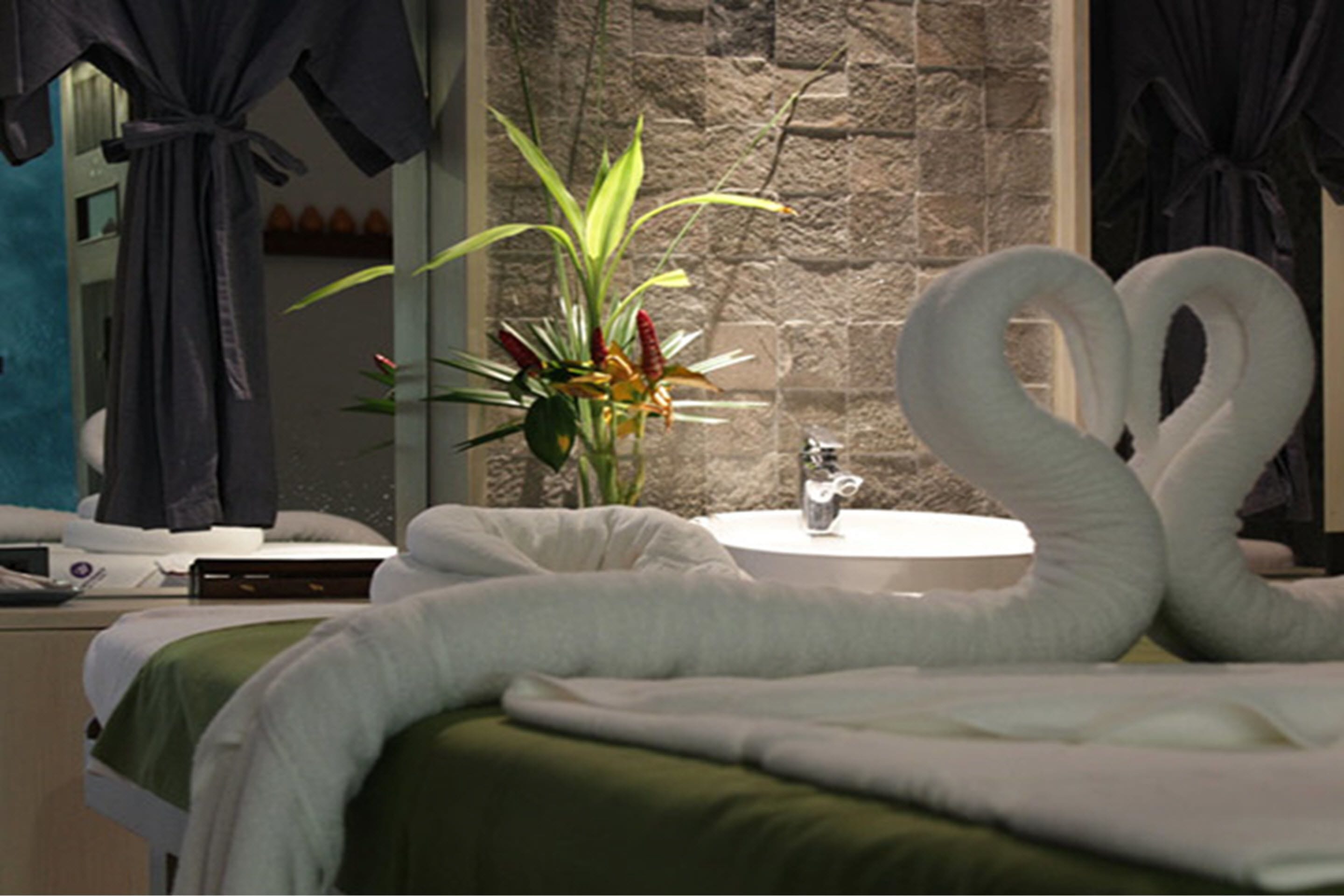 A hotel room with a bed, a round white sink, and a decorative swan-shaped towel.