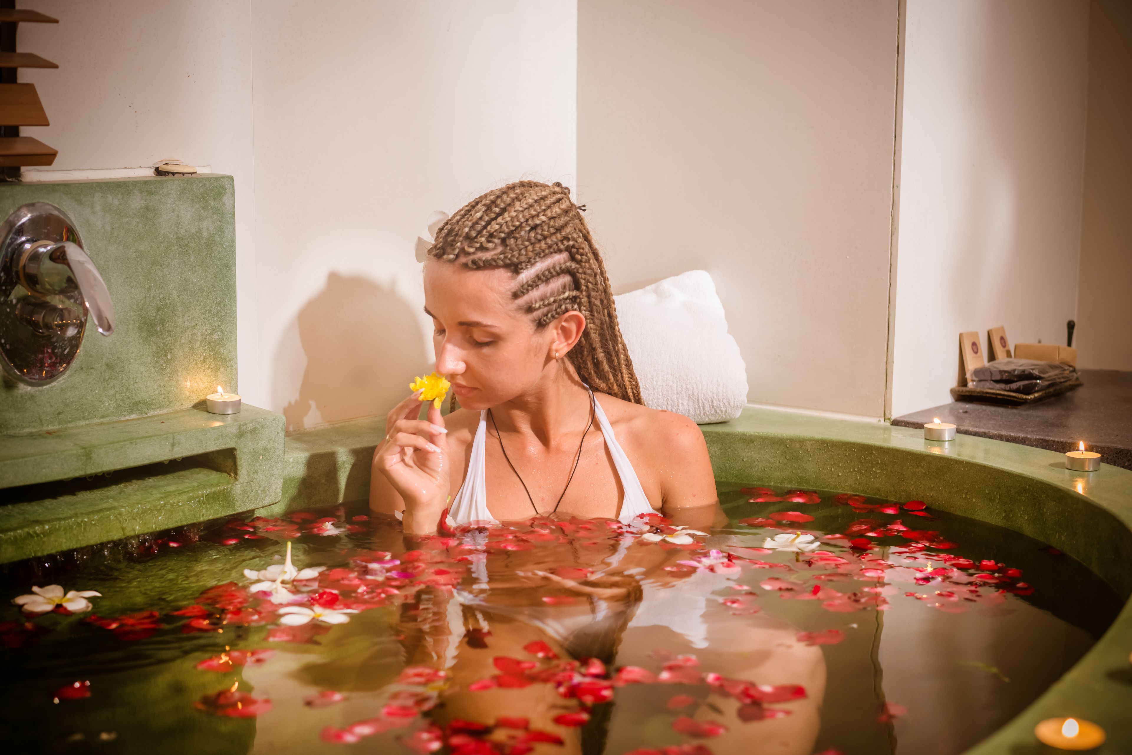 A person in a bathtub with water lilies and candles.