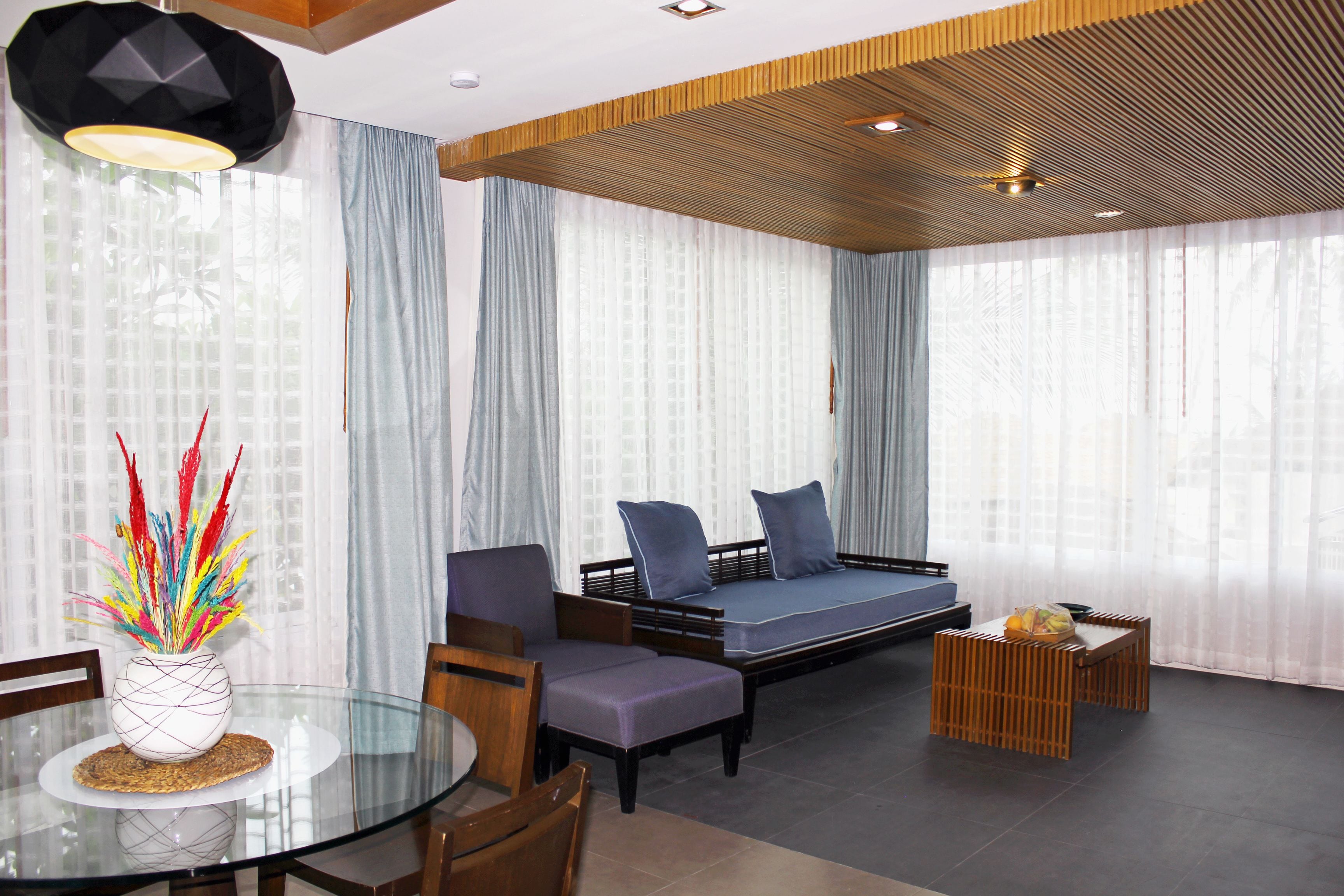 A modern living room with a glass dining table, a sofa, and a small wooden table.