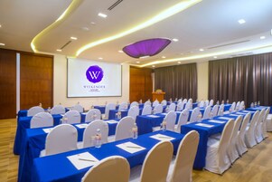 Un salón de conferencias con filas de mesas, sillas blancas y una pantalla de presentación que muestra 'WEEKENDER RESORT'.