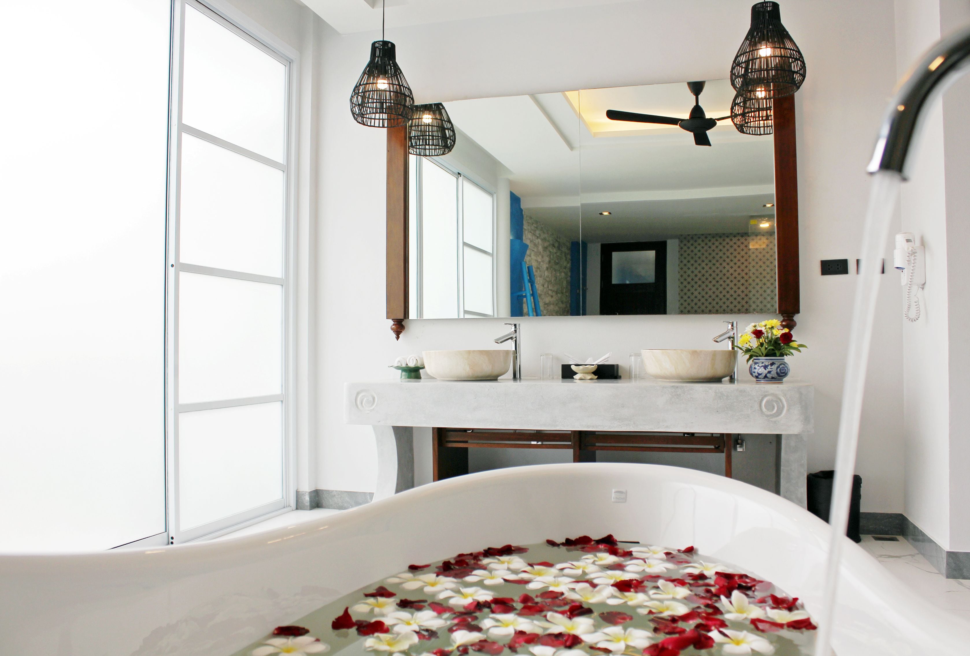 A bathroom with a bathtub filled with rose petals, a large mirror, and two pendant lights.