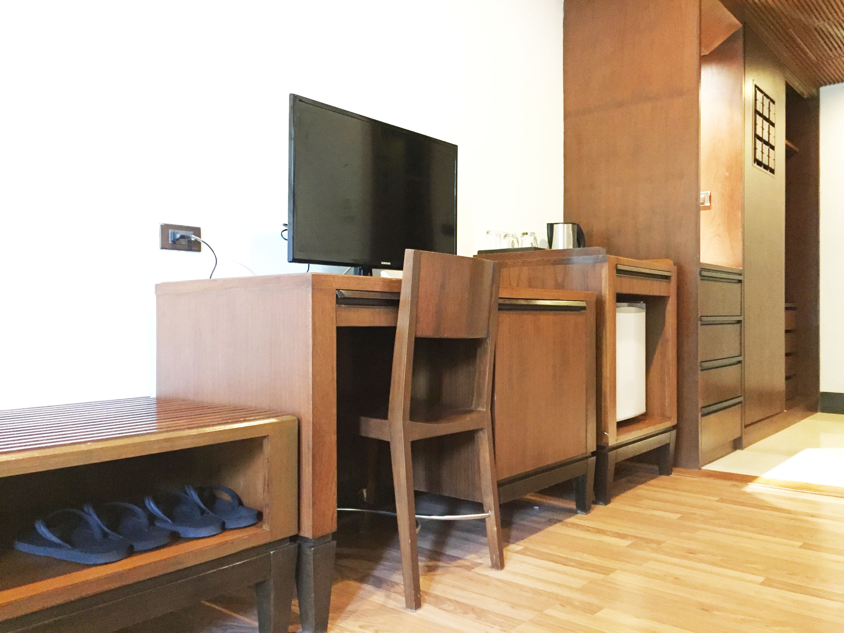 Un bureau en bois, une télévision, une chaise et un porte-chaussures avec des chaussons.