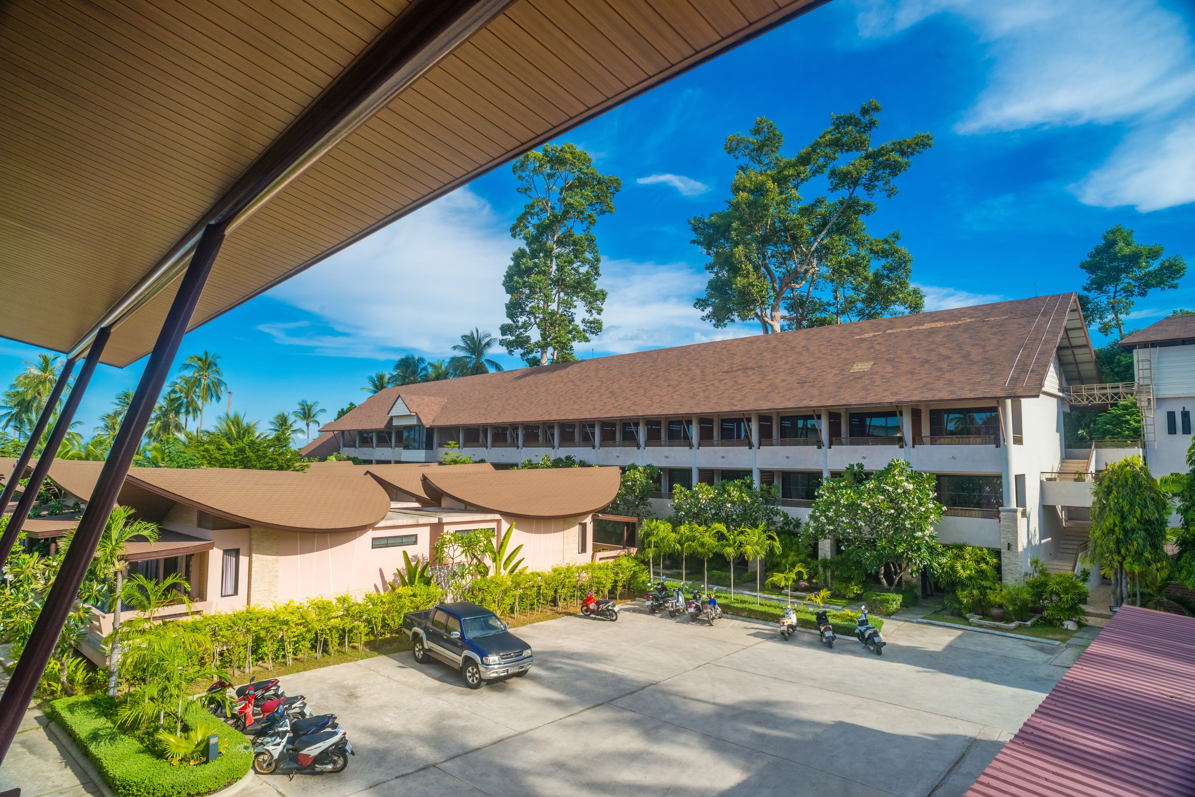 A hotel with a covered parking area, multiple buildings, and surrounding greenery.