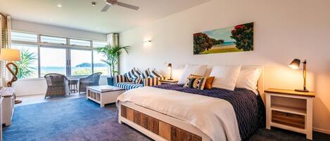 A bedroom with a large bed, a seating area with a view, and a ceiling fan.