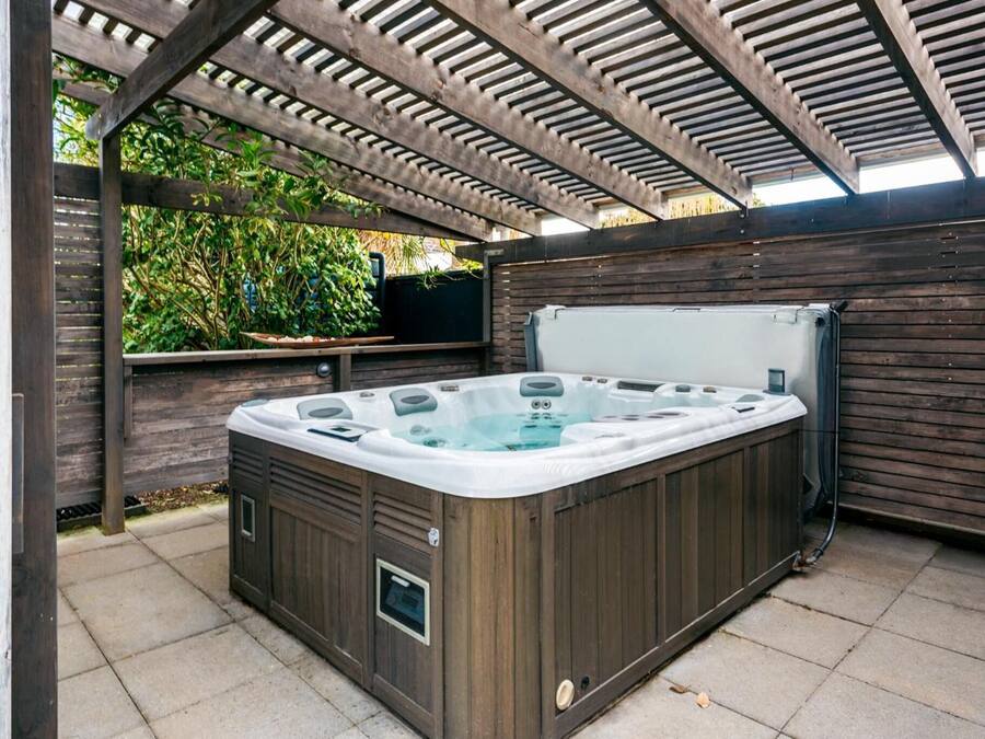 A hot tub in an outdoor patio area with a wooden pergola overhead.