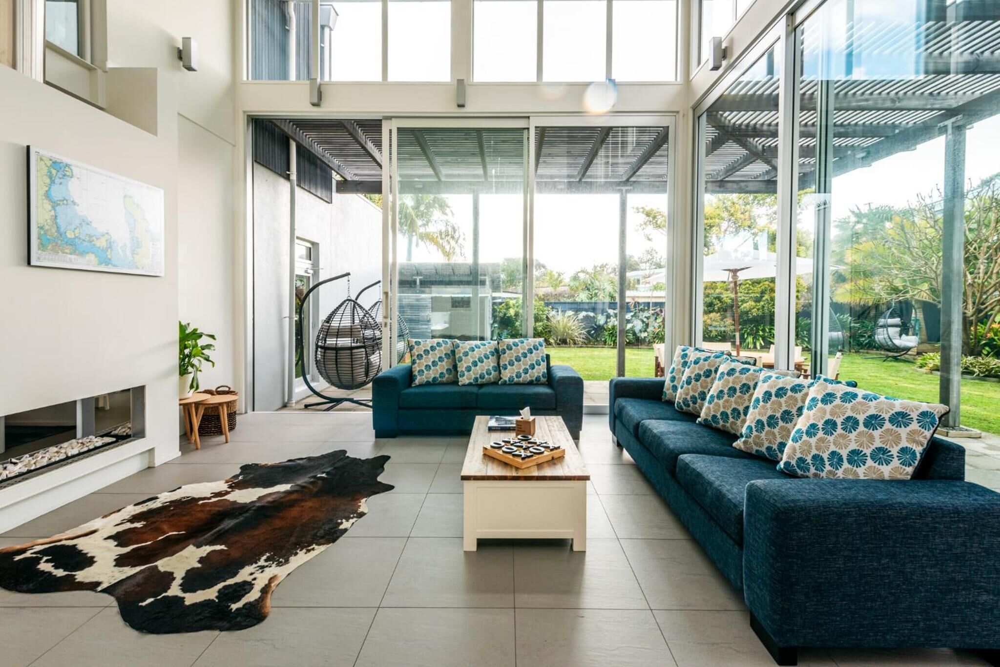 A modern living room with a large glass door leading to a garden, a blue sofa set, a wooden coffee table, and a cowhide rug.