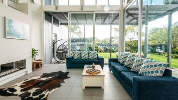 A modern living room with a large glass door leading to a garden, a blue sofa set, a wooden coffee table, and a cowhide rug.