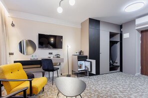 A modern hotel room with a sofa, a chair, a desk, a flat-screen TV, a mirror, a wardrobe, and a mini-fridge. - Hotel Tarnovia (Tarnow)