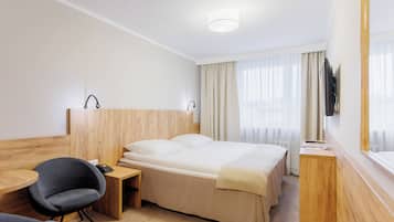 A hotel room with a bed, bedside table, chair, desk, and a TV mounted on the wall.
