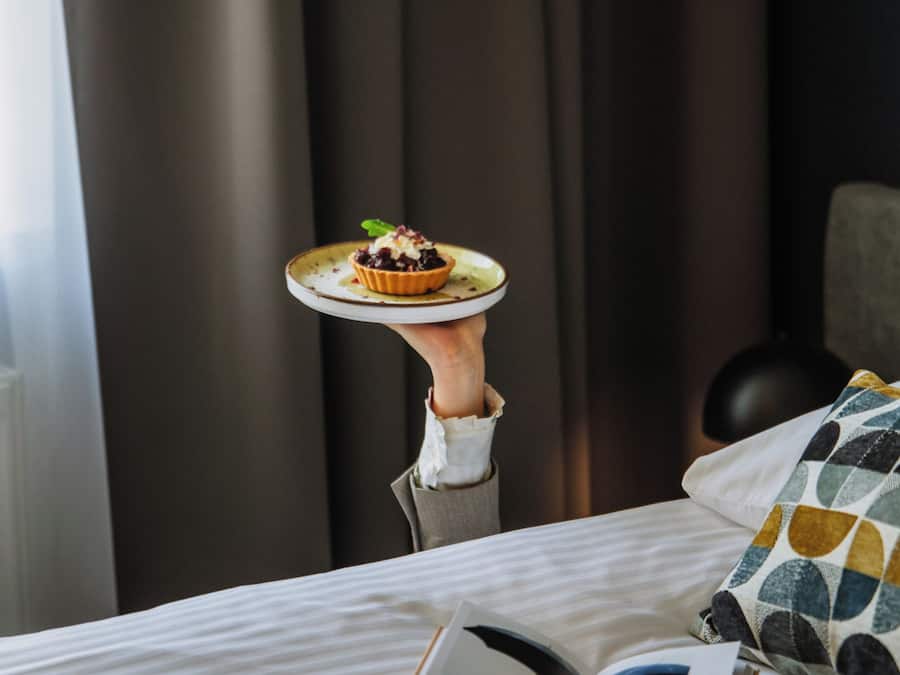 Un lit avec un livre, une assiette avec de la nourriture et une lampe dans une pièce avec des rideaux.