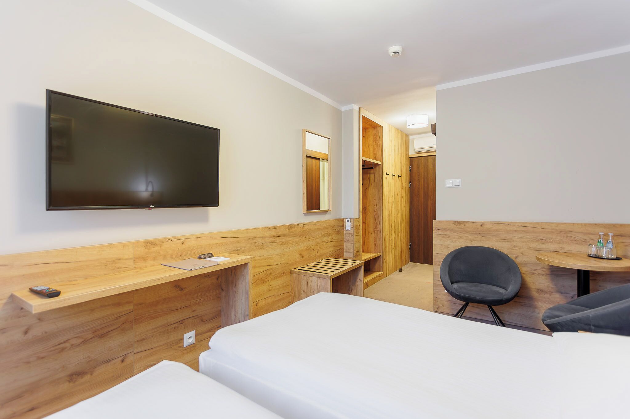 Une chambre d’hôtel comprenant un lit, un bureau, une chaise, une télévision et une armoire en bois.