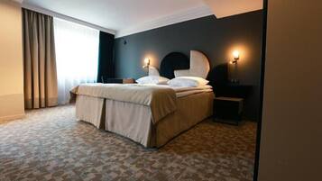 Una habitación de hotel con cama, mesita de noche, lámpara y un amplio ventanal con cortinas.