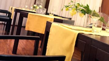 Un restaurante con mesas dispuestas, cubiertas con manteles amarillos, copas de vino y centros de mesa florales.