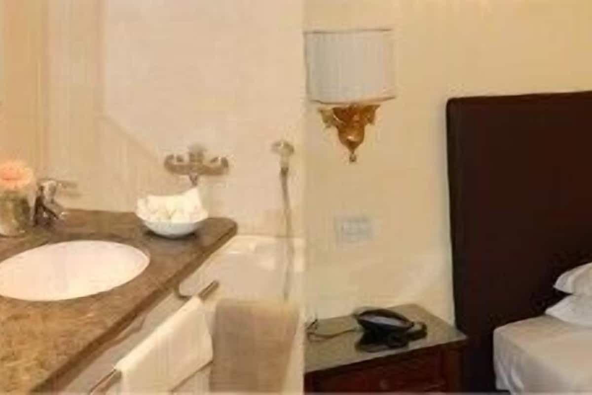 A hotel room with a bed, a bedside table, a lamp, and a bathroom with a sink and mirror.