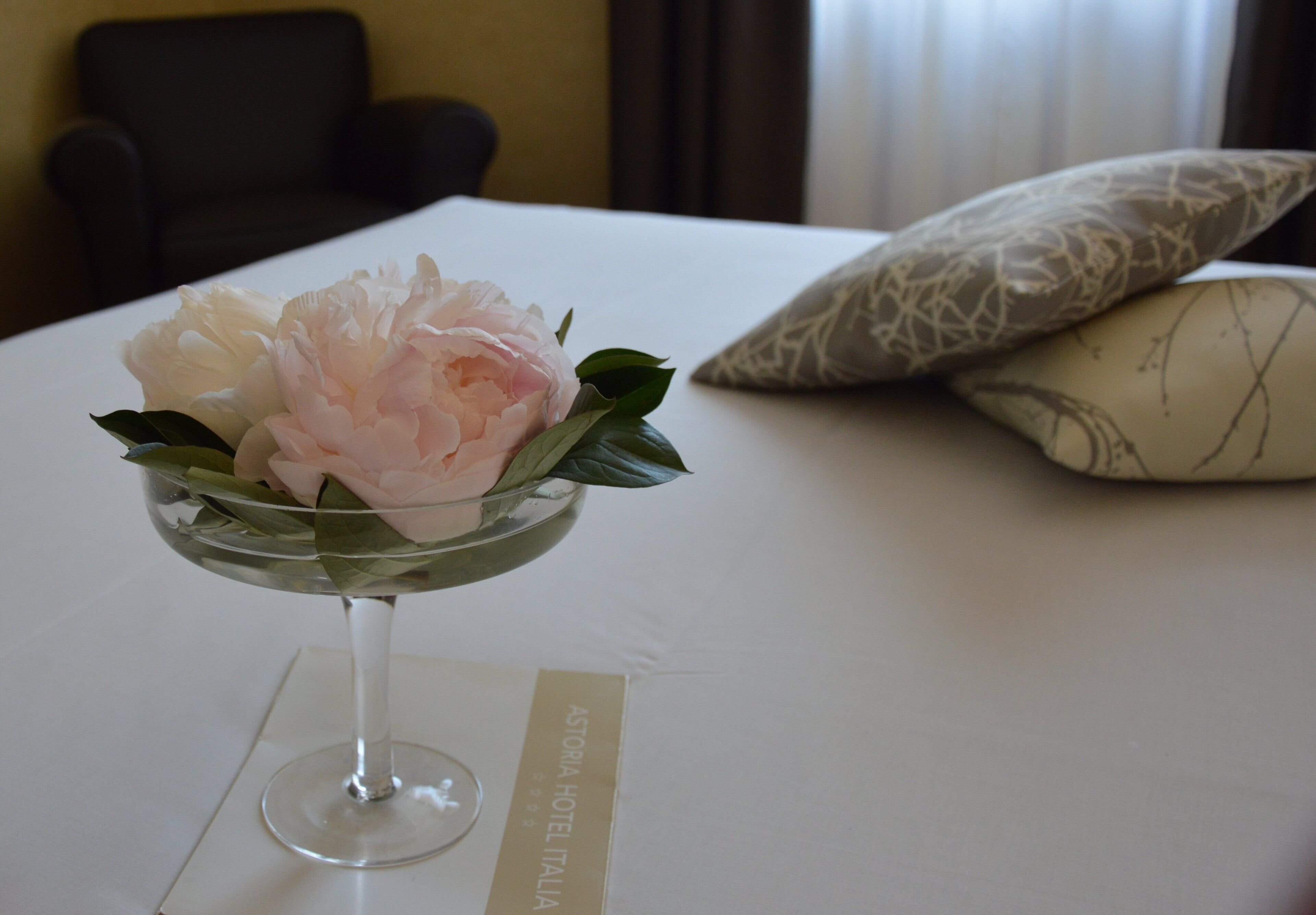 A bed with a white bedspread, a decorative glass bowl with flowers, and a pillow with a geometric pattern.