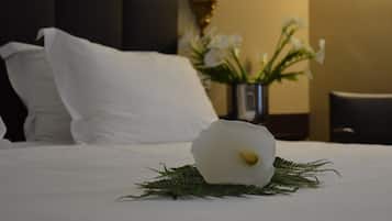 Ein ordentlich bezogenes Bett mit weißen Leinen, eine weiße Blumenarragemnt und eine Vase mit weißen Blumen im Hintergrund.