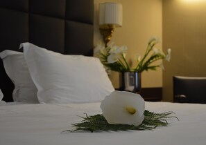 Restful retreat with a neatly made bed, adorned with a single white flower and greenery, and a bedside lamp.