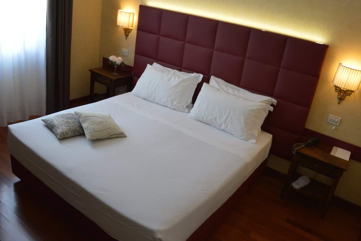 A hotel room with a large bed, two bedside tables, a nightstand, and a wall-mounted lamp.