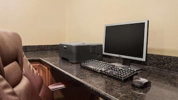 A hotel workspace with a leather chair, a desktop computer, a keyboard, a mouse, and a printer.