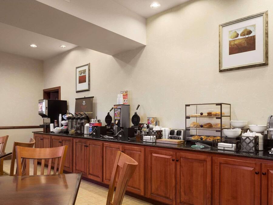 Una barra de desayuno con armarios de madera, una cafetera y diversos alimentos para el desayuno.