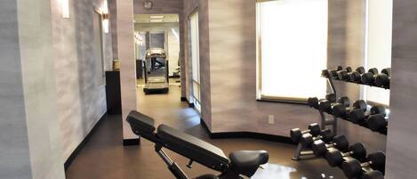 Ein Fitnessstudio mit Trainingsgeräten, darunter eine Bank und Kurzhanteln, sowie ein großes Fenster, das für natürliches Licht sorgt.