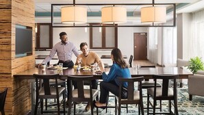 Een moderne hotel eetruimte met een lange tafel, meerdere stoelen en een groot raam dat natuurlijk licht binnenlaat.