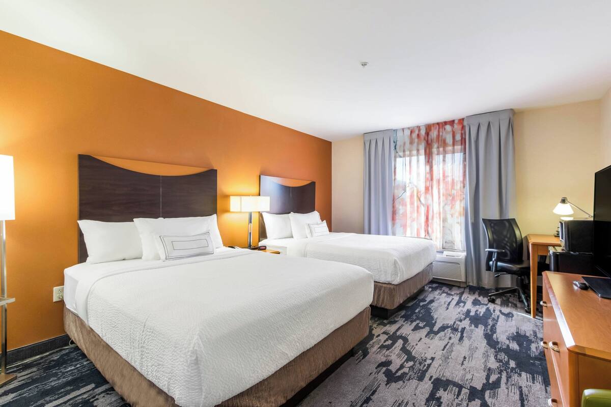 Una habitación de hotel con dos camas, un escritorio, una silla y un televisor.